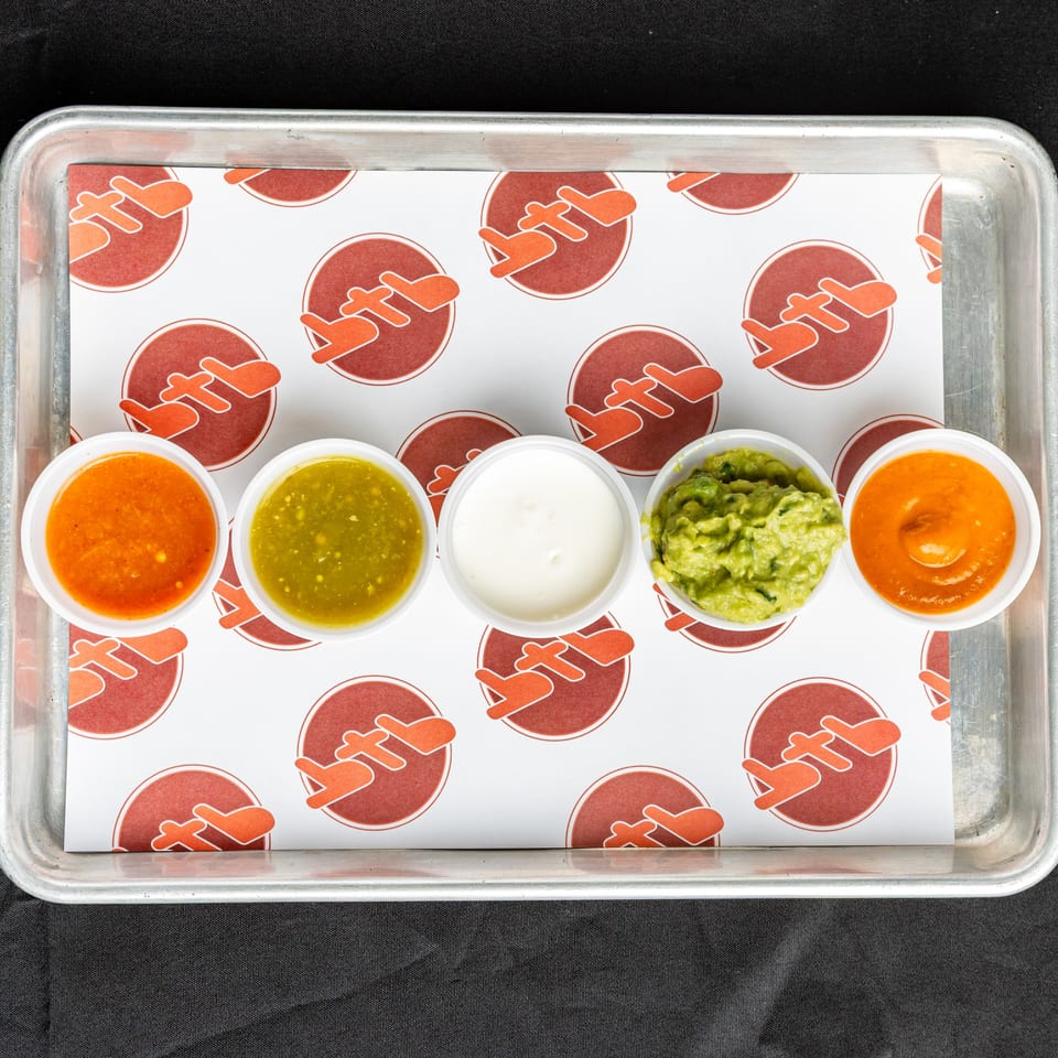 Five small cups of BTB Burrito's Mexican sauces, including salsa, guacamole, and sour cream.