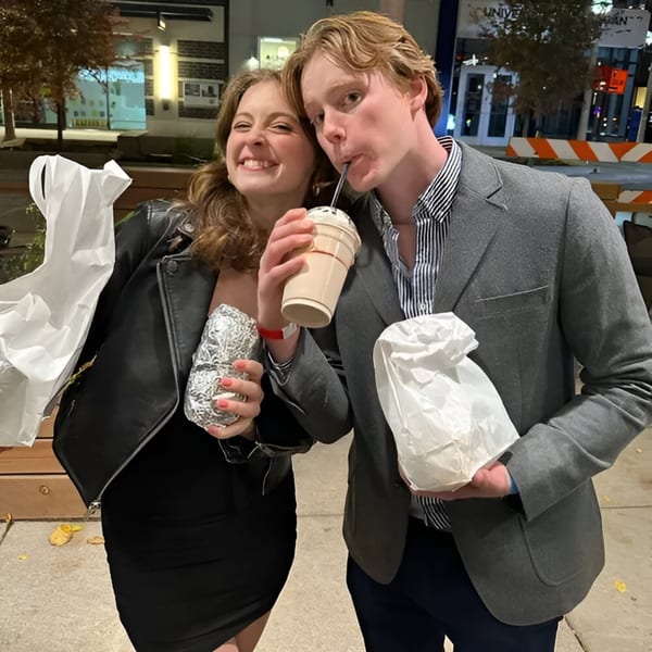 Two happy customers, a woman and a man, holding BTB Burrito food and a drink at night.