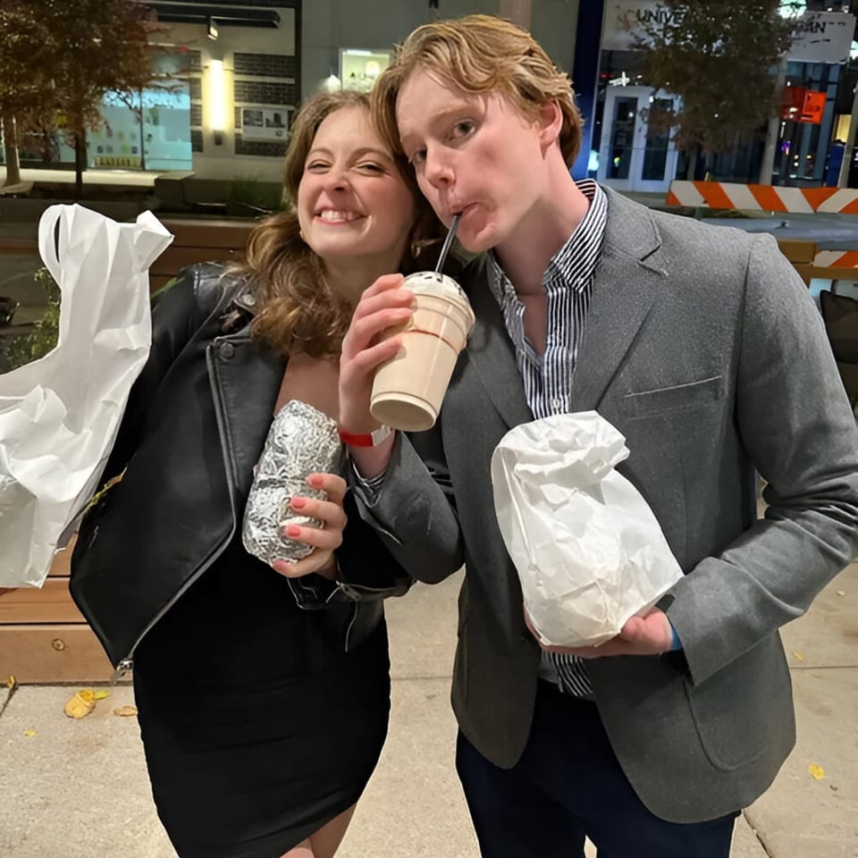 Two happy customers, a woman and a man, holding BTB Burrito food and a drink at night.