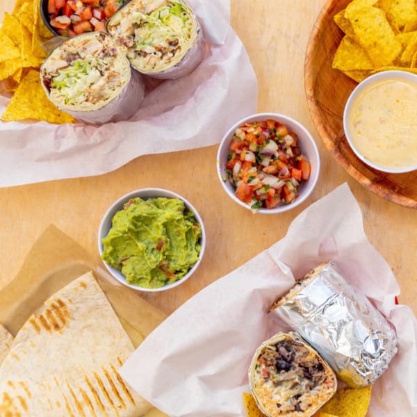 BTB Burrito spread with burritos, quesadillas, chips, salsa, guacamole, and queso on a wooden table.