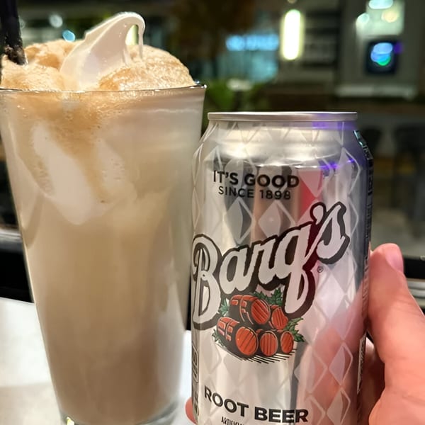 A Barq's Root Beer can next to a tall glass of root beer float with a straw.