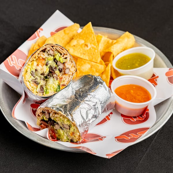 Two BTB Burritos, one cut open, with tortilla chips and two dipping sauces on a metal tray.